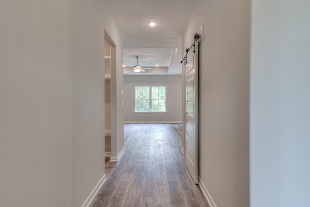 hallway featuring dark wood-type flooring, a barn door, a raised ceiling, and a textured ceiling