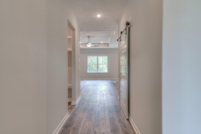 hall with a barn door, hardwood / wood-style floors, a textured ceiling, and a tray ceiling