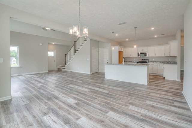 kitchen featuring light hardwood / wood-style flooring, appliances with stainless steel finishes, white cabinetry, hanging light fixtures, and a kitchen island with sink