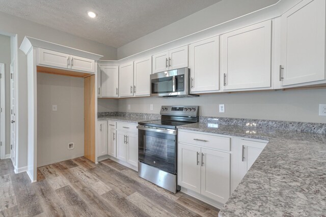 kitchen with appliances with stainless steel finishes, light hardwood / wood-style floors, and white cabinets