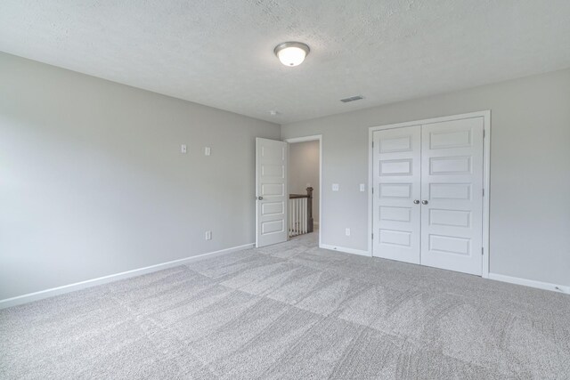 unfurnished bedroom with light carpet, a closet, and a textured ceiling