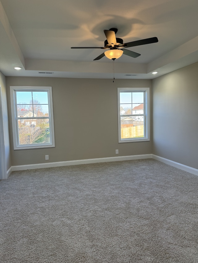 empty room featuring plenty of natural light, carpet floors, ceiling fan, and a tray ceiling