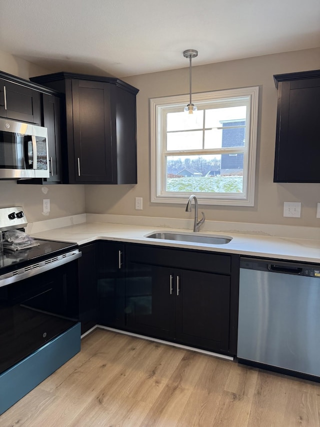 kitchen featuring decorative light fixtures, light hardwood / wood-style floors, sink, and appliances with stainless steel finishes