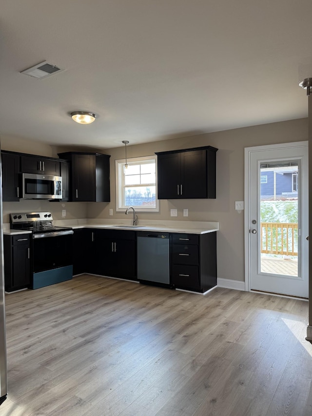 kitchen featuring hanging light fixtures, sink, light hardwood / wood-style flooring, and appliances with stainless steel finishes