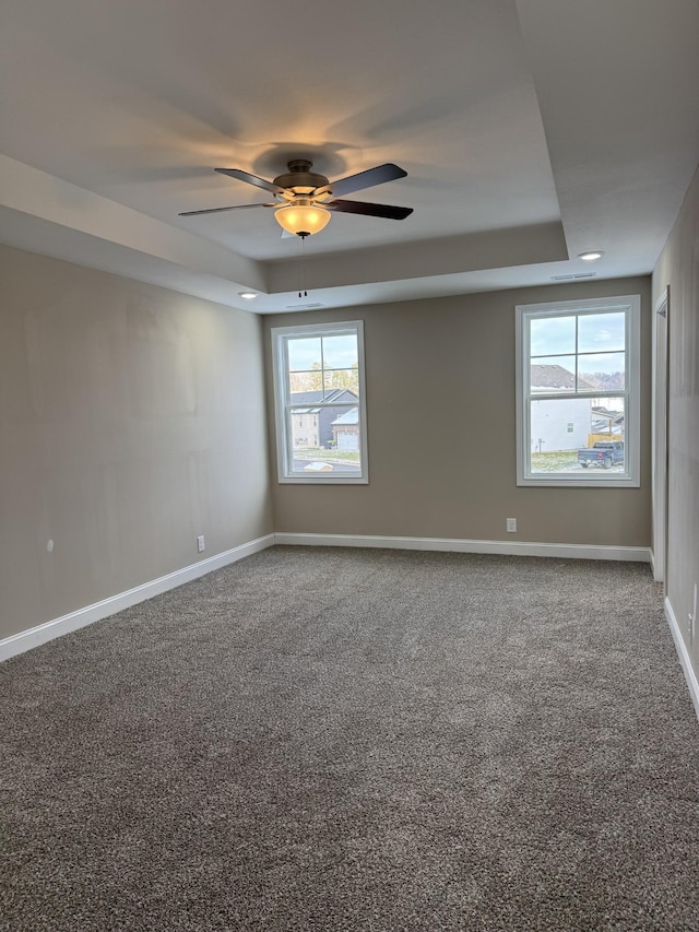 carpeted spare room with a tray ceiling and ceiling fan