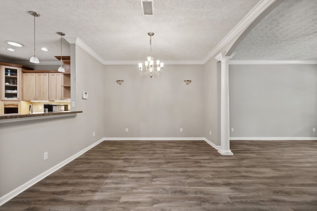 unfurnished dining area with a textured ceiling, an inviting chandelier, dark wood-type flooring, ornate columns, and ornamental molding