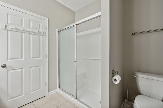 bathroom with tile patterned flooring, a shower with door, toilet, and a textured ceiling