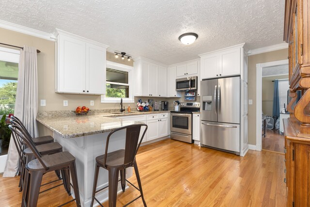 kitchen featuring light wood-type flooring, stainless steel appliances, ornamental molding, and light stone counters