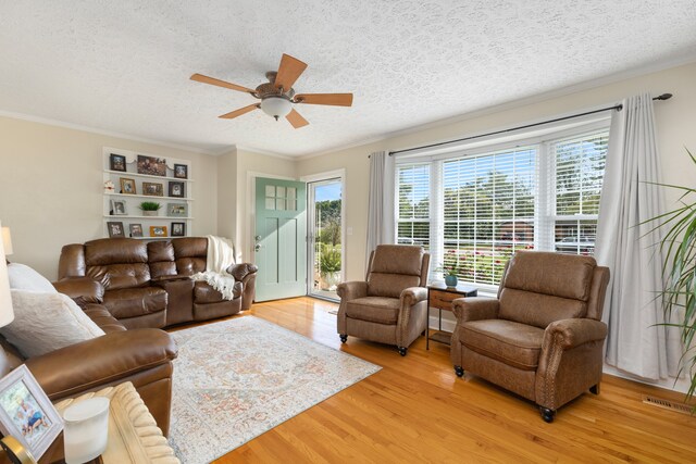 living room with a textured ceiling, ceiling fan, crown molding, and light wood-type flooring