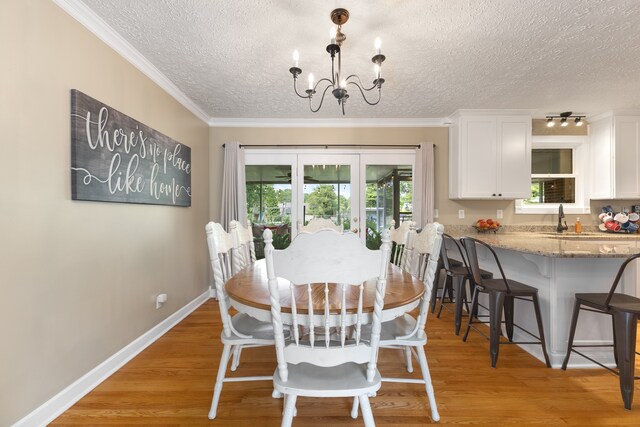 dining space with sink, a notable chandelier, ornamental molding, light hardwood / wood-style floors, and a textured ceiling