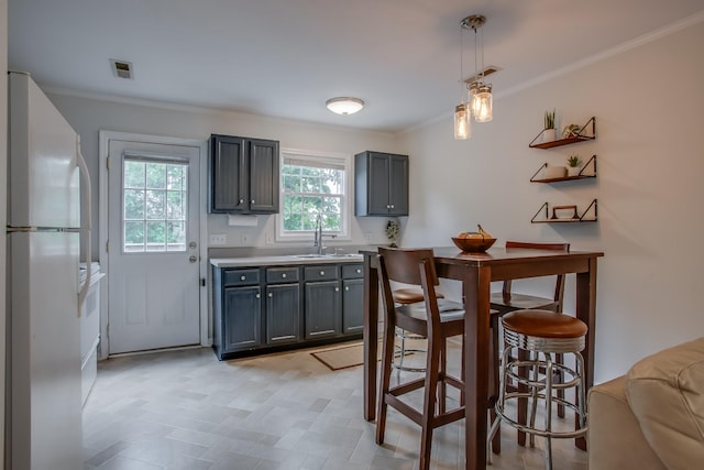 kitchen featuring hanging light fixtures, crown molding, sink, and white refrigerator