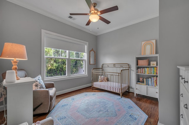 bedroom featuring dark hardwood / wood-style flooring, a nursery area, crown molding, and ceiling fan