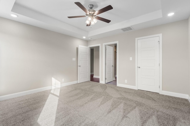 unfurnished bedroom with a raised ceiling, ceiling fan, and carpet