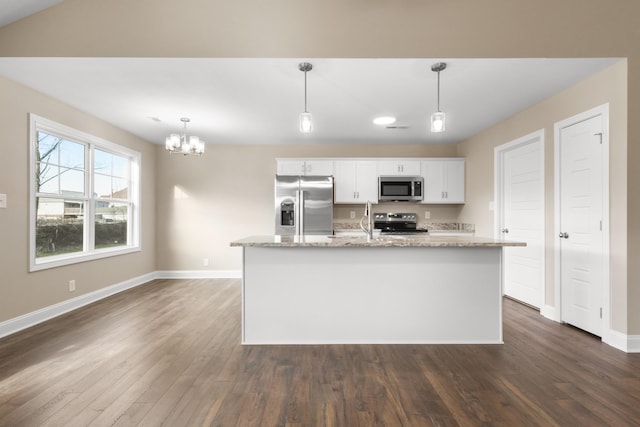 kitchen with light stone countertops, decorative light fixtures, stainless steel appliances, an island with sink, and white cabinets