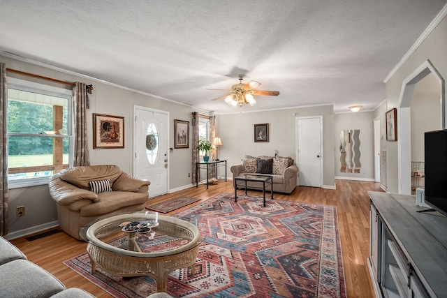 living room with light hardwood / wood-style flooring, a textured ceiling, ornamental molding, and ceiling fan