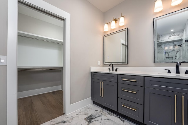 bathroom with marble finish floor, a spacious closet, baseboards, and a sink