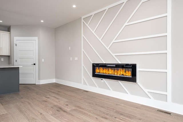 room details with recessed lighting, visible vents, a glass covered fireplace, wood finished floors, and baseboards