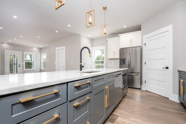 kitchen with stainless steel appliances, white cabinets, sink, hanging light fixtures, and light wood-type flooring