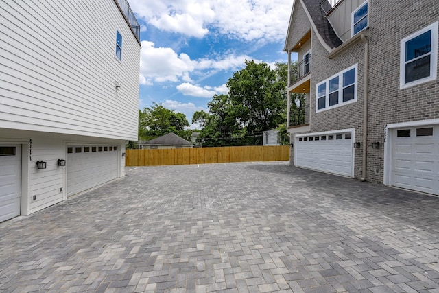 view of property exterior with a garage, fence, decorative driveway, and brick siding