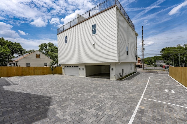 view of side of property with decorative driveway, an attached garage, and fence