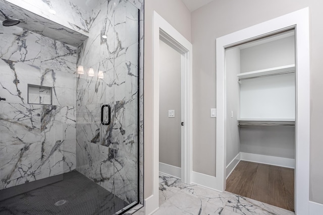 full bathroom with marble finish floor, a walk in closet, a marble finish shower, and baseboards