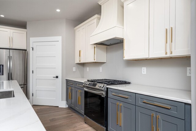 kitchen with custom range hood, white cabinets, light stone countertops, appliances with stainless steel finishes, and wood-type flooring