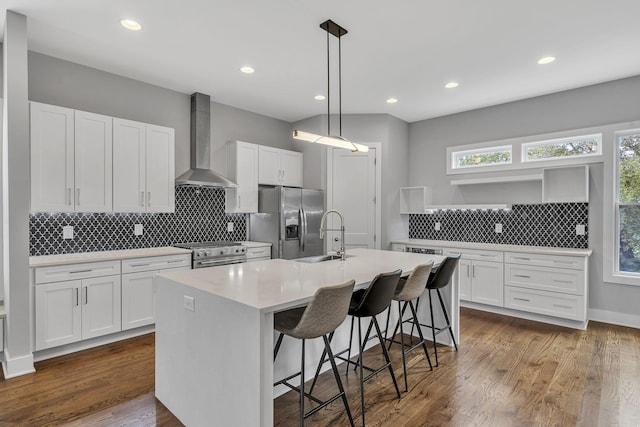 kitchen with appliances with stainless steel finishes, wall chimney exhaust hood, an island with sink, and white cabinets