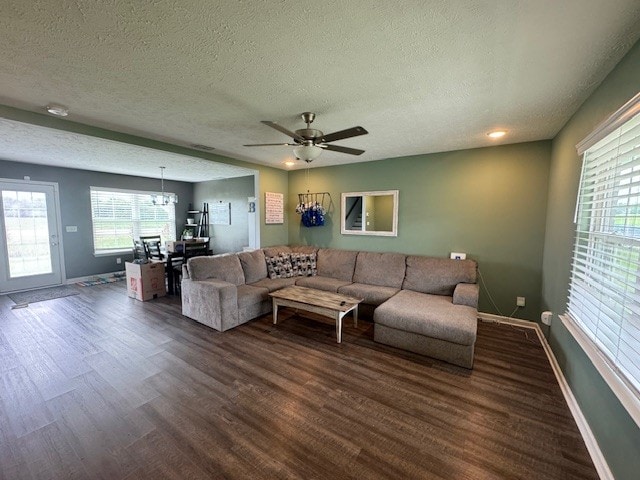 living room with ceiling fan with notable chandelier, a textured ceiling, and dark wood-type flooring