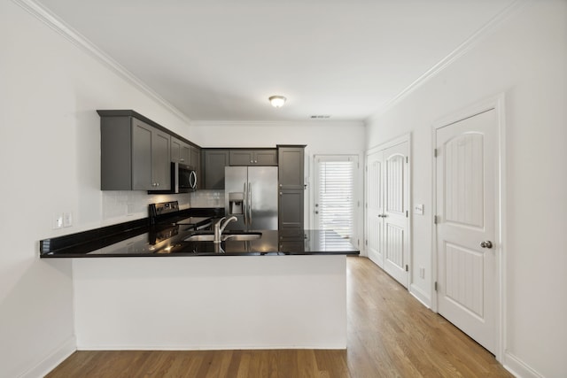 kitchen with stainless steel appliances, sink, ornamental molding, light hardwood / wood-style flooring, and kitchen peninsula