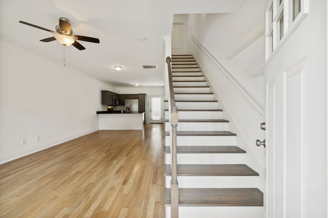 stairway featuring light wood-type flooring, crown molding, and ceiling fan