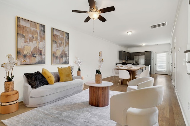 living room with ceiling fan, wood-type flooring, and crown molding