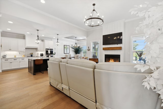 living room with light wood-type flooring, a large fireplace, an inviting chandelier, and ornamental molding