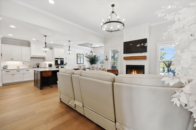 living area featuring a fireplace, crown molding, recessed lighting, an inviting chandelier, and light wood-style floors