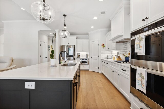 kitchen with sink, crown molding, an island with sink, and stainless steel appliances