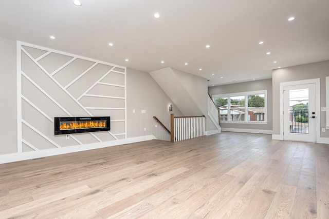 unfurnished living room featuring a glass covered fireplace, light wood-style flooring, baseboards, and recessed lighting