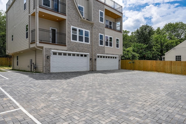 exterior space featuring decorative driveway, brick siding, fence, and an attached garage