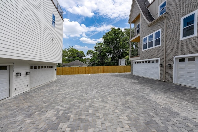 view of side of property with a garage, brick siding, decorative driveway, and fence