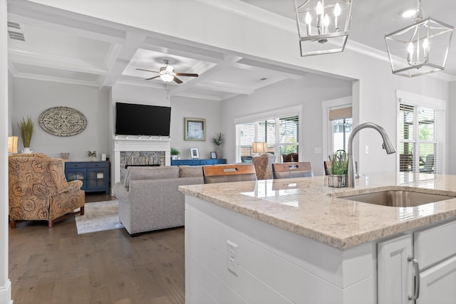 kitchen with white cabinets, ceiling fan with notable chandelier, a stone fireplace, sink, and plenty of natural light