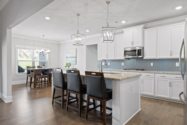 kitchen with hanging light fixtures, dark hardwood / wood-style floors, an island with sink, and white cabinets