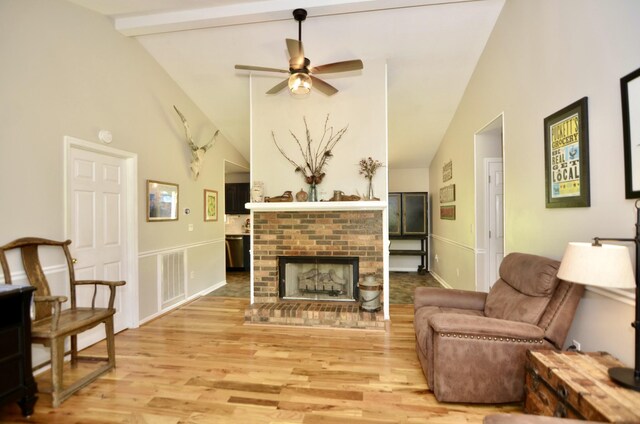 living room featuring a fireplace, high vaulted ceiling, beamed ceiling, ceiling fan, and light hardwood / wood-style flooring