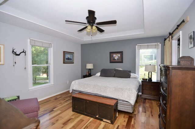 bedroom with ceiling fan, a barn door, light hardwood / wood-style flooring, and multiple windows