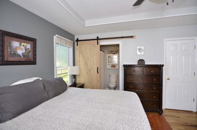 bedroom with ceiling fan, a barn door, ensuite bath, and hardwood / wood-style floors