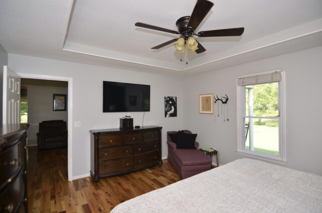 bedroom with ceiling fan, a raised ceiling, and dark hardwood / wood-style flooring