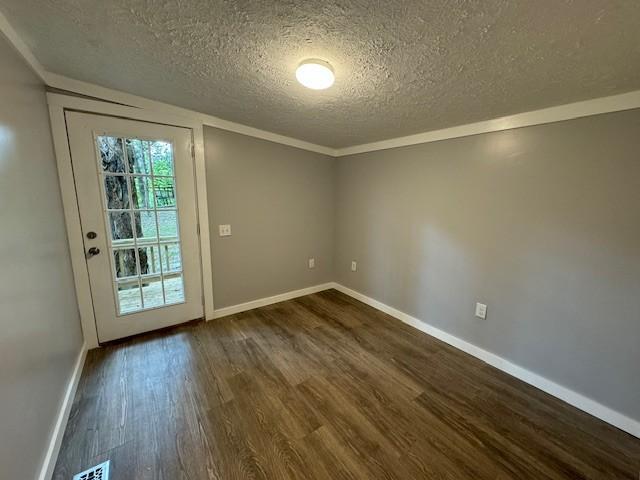 doorway to outside with crown molding, dark wood-type flooring, and a textured ceiling