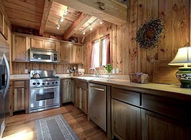 kitchen with wooden walls, light hardwood / wood-style flooring, stainless steel appliances, and beam ceiling