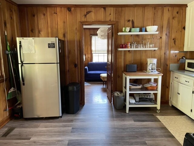 kitchen with wood walls, stainless steel fridge, and wood-type flooring