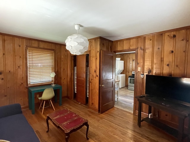 living room featuring stacked washer and dryer, wooden walls, and light hardwood / wood-style flooring