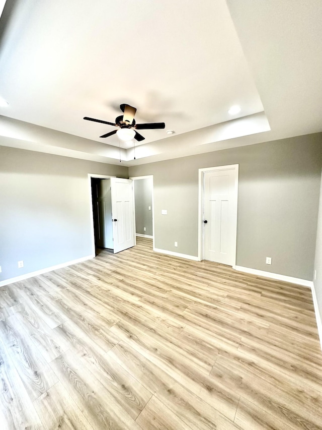 unfurnished bedroom with ceiling fan, a tray ceiling, and light hardwood / wood-style floors