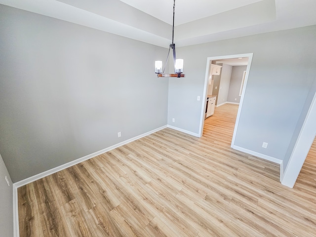 unfurnished dining area featuring a notable chandelier, a tray ceiling, and light hardwood / wood-style flooring