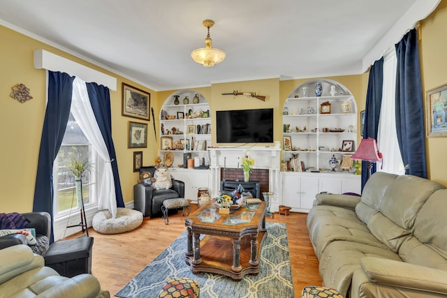 living room featuring built in features, a brick fireplace, and wood-type flooring